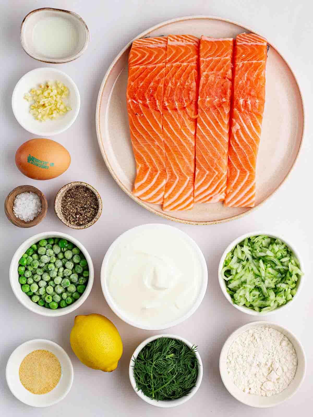 Burger di Salmone Fresco {con Salsa Tzatziki} 4 Gli ingredienti per i burger di salmone disposti su un piano di lavoro in piatti e piccole ciotole.