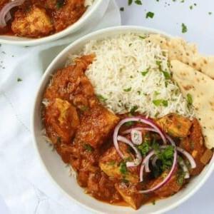 Curry di Pollo Facile {Rapido e Sano} 4 Due ciotole di pollo al curry e riso su una tovaglia bianca.