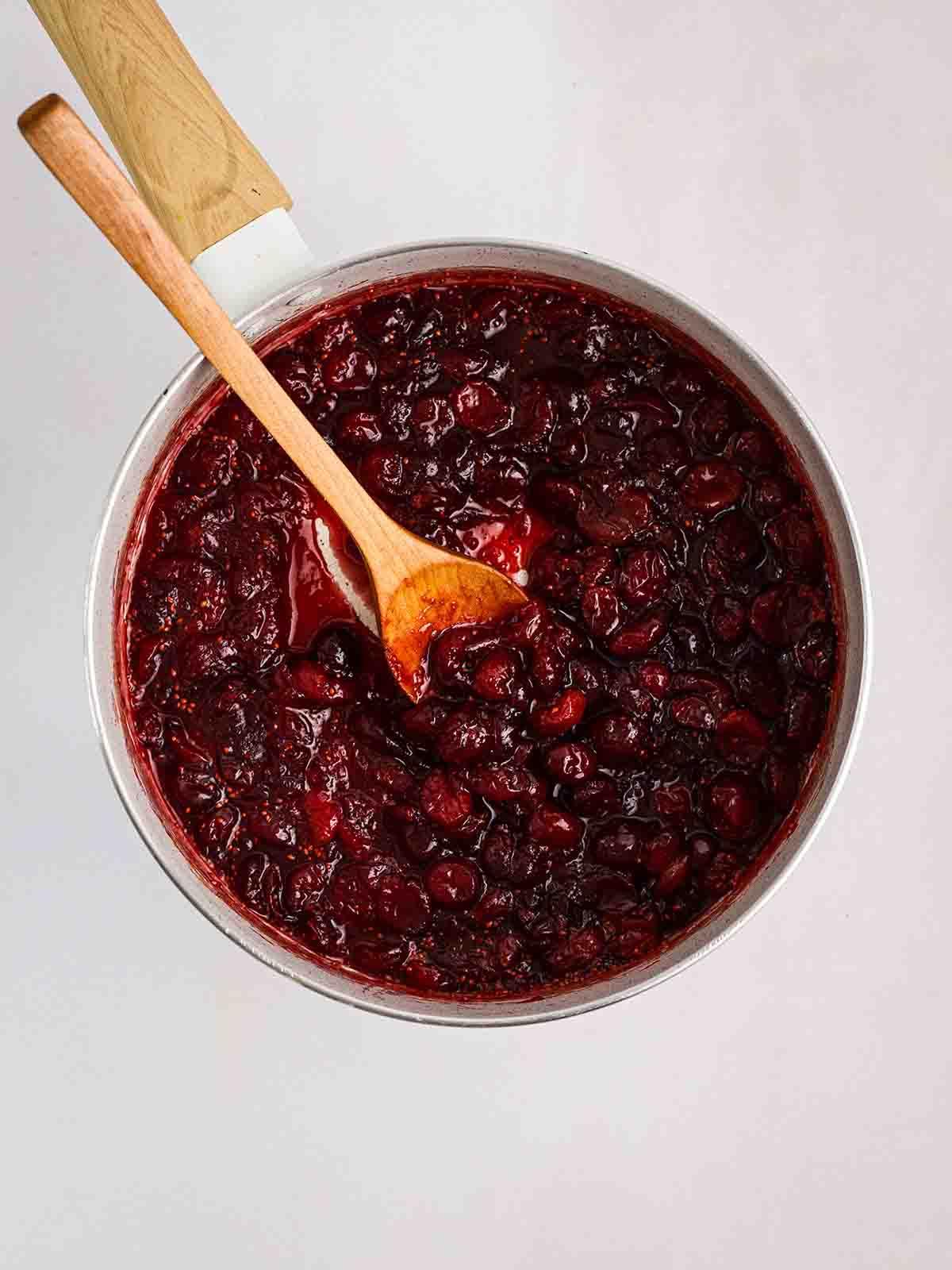 Salsa di Mirtilli Rossi Fatta in Casa 5 Salsa ai mirtilli rossi in una pentola con un cucchiaio di legno, mentre si mescola.