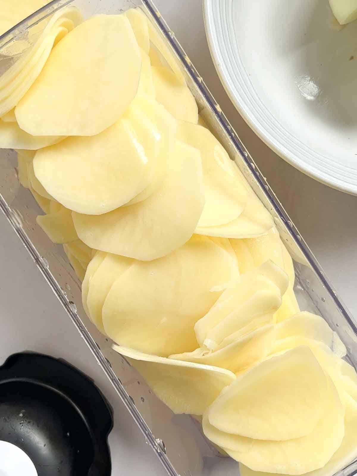 Patate alla Boulangère 5 Patate finemente affettate in un contenitore, pronte per preparare le Patate alla Boulangère.