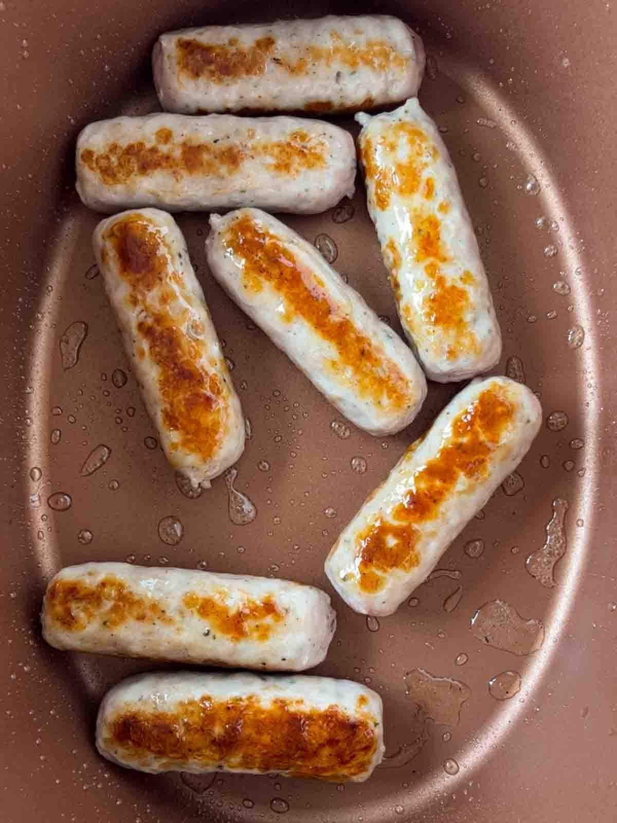 Stufato di Salsicce a Cottura Lenta {Ricetta Facile} 5 Sausages frying in a slow cooker for the recipe Sausage Casserole.