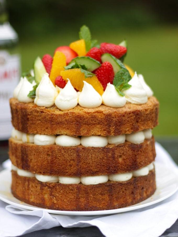La Ricetta Definitiva della Torta al Pimms 6 Pimms cake con glassa, cetriolo, fragole, arance e menta su un piatto bianco in giardino, ricetta torta al Pimms.
