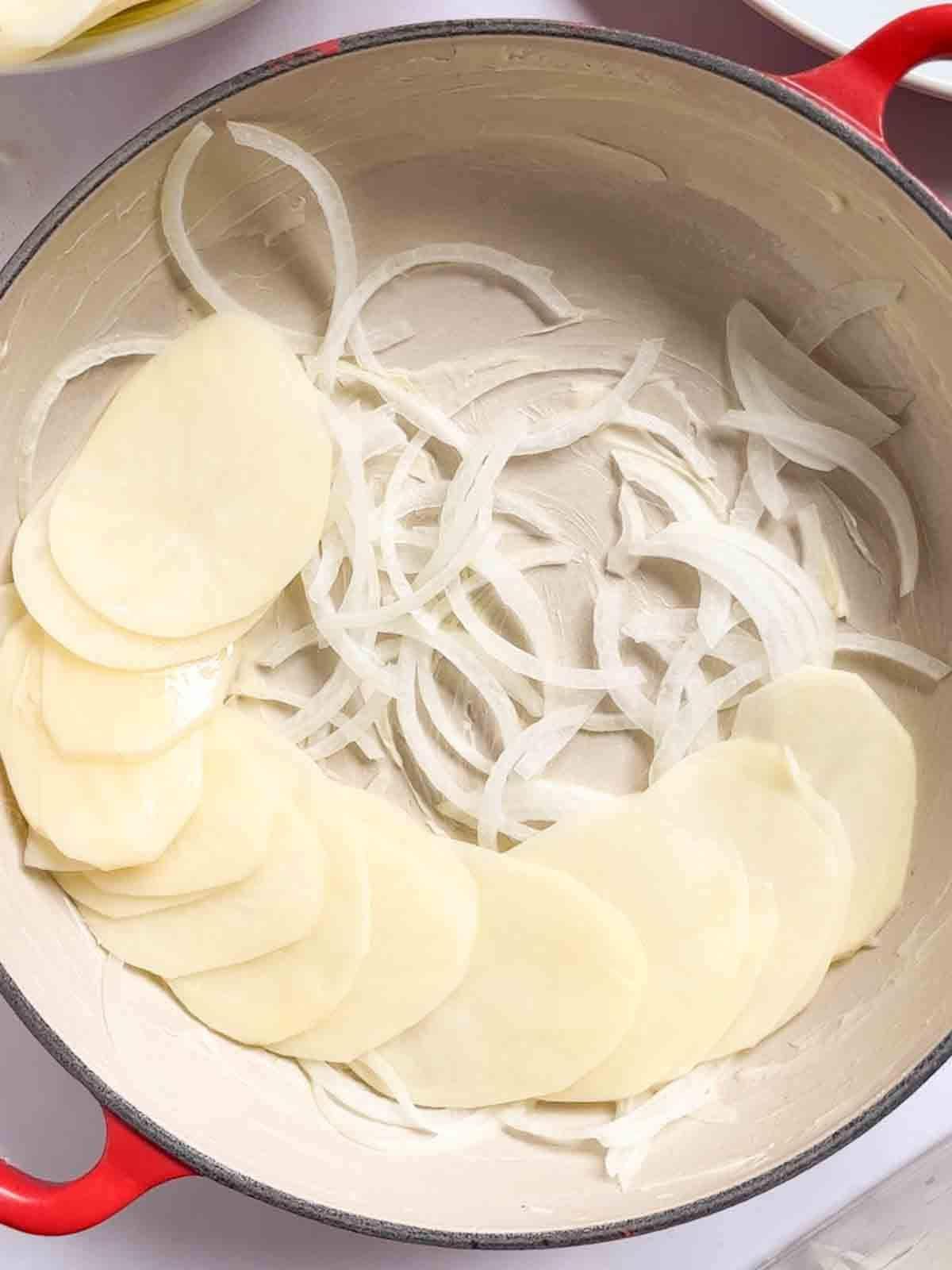 Patate alla Boulangère 6 Cipolle sul fondo di una teglia pesante con fette di patate per il passaggio 2 della ricetta delle Patate alla Boulangère.