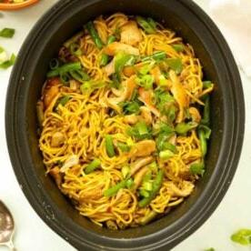 Piano Pasti 20 7 Una pentola slow cooker nera piena di noodles al curry e pollo, con fagiolini.