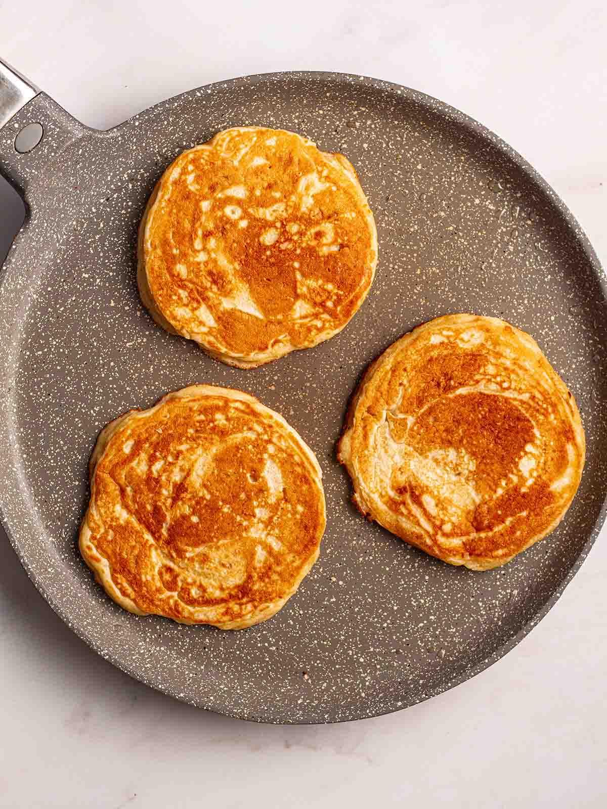 Pancakes Americani {Ricetta Facile!} 8 Una padella con 3 Pancakes Americani rotondi in cottura per il passaggio 4 del processo della ricetta.