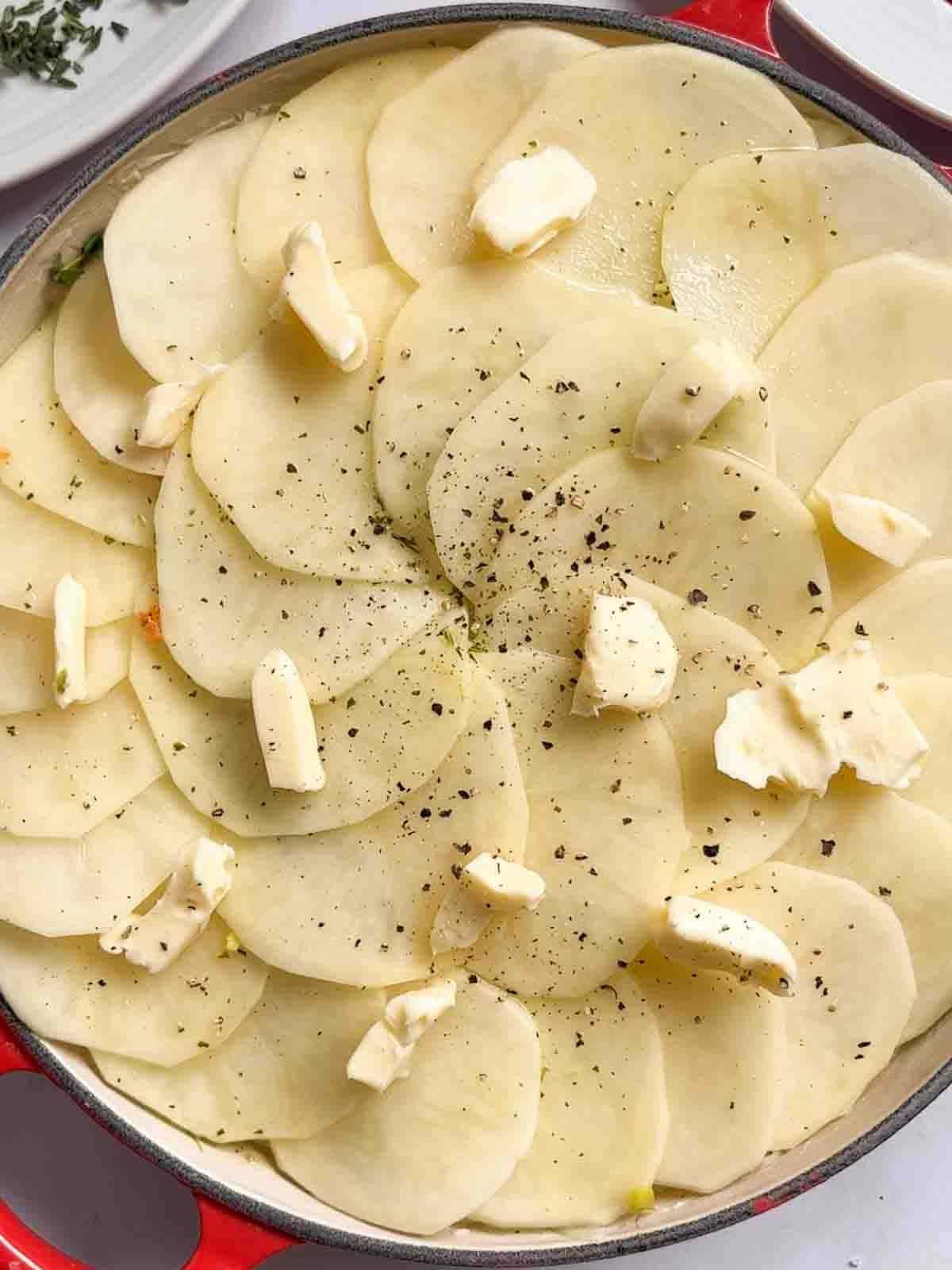 Patate alla Boulangère 8 Rondelle di patate affettate con fiocchetti di burro e pepe nero sopra, per il passaggio 4 della ricetta delle Patate alla Boulangère.