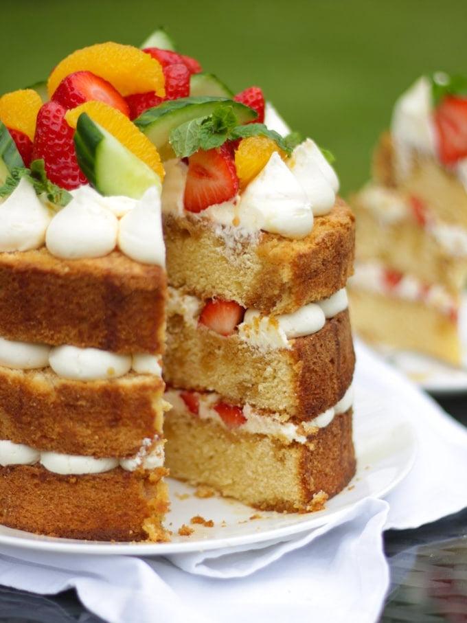 La Ricetta Definitiva della Torta al Pimms 8 Pimms cake con glassa, cetriolo, fragole, arance e menta su un piatto bianco in giardino, ricetta torta al Pimms.