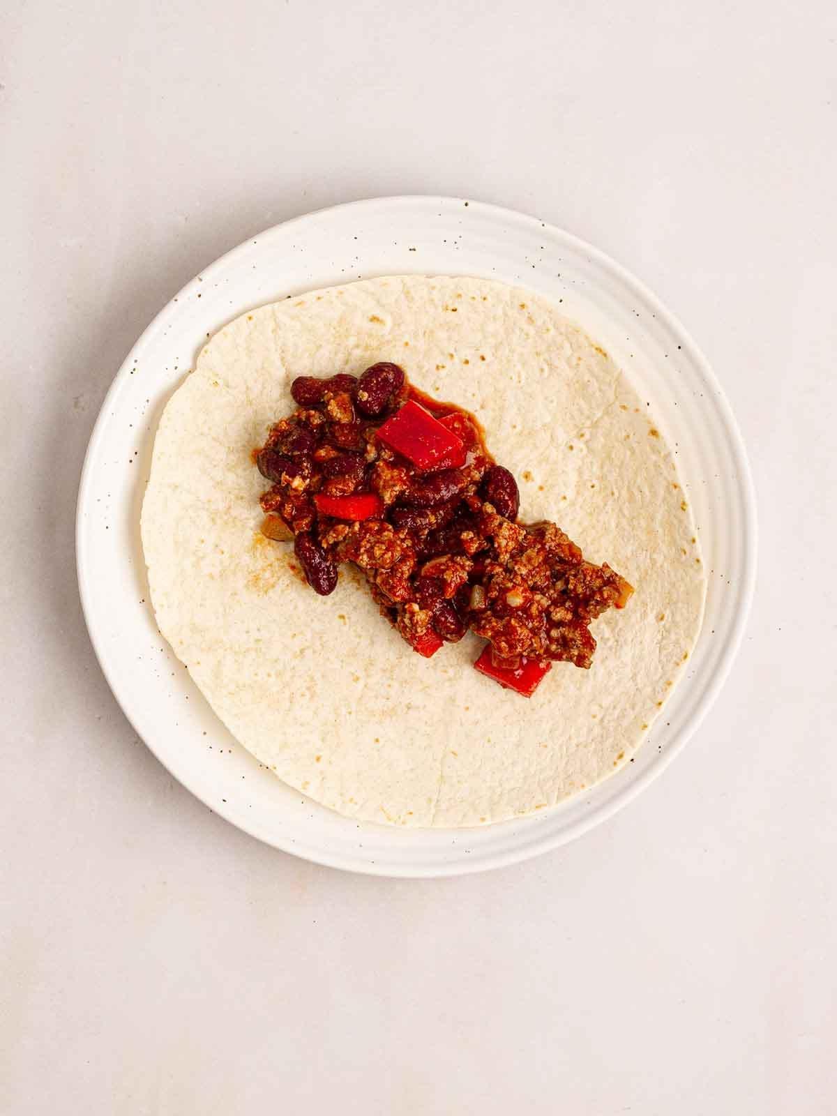 Enchiladas di Manzo 8 Un piatto con una tortilla e carne macinata al chili al centro per il passo 4 della ricetta delle Enchiladas di Manzo.