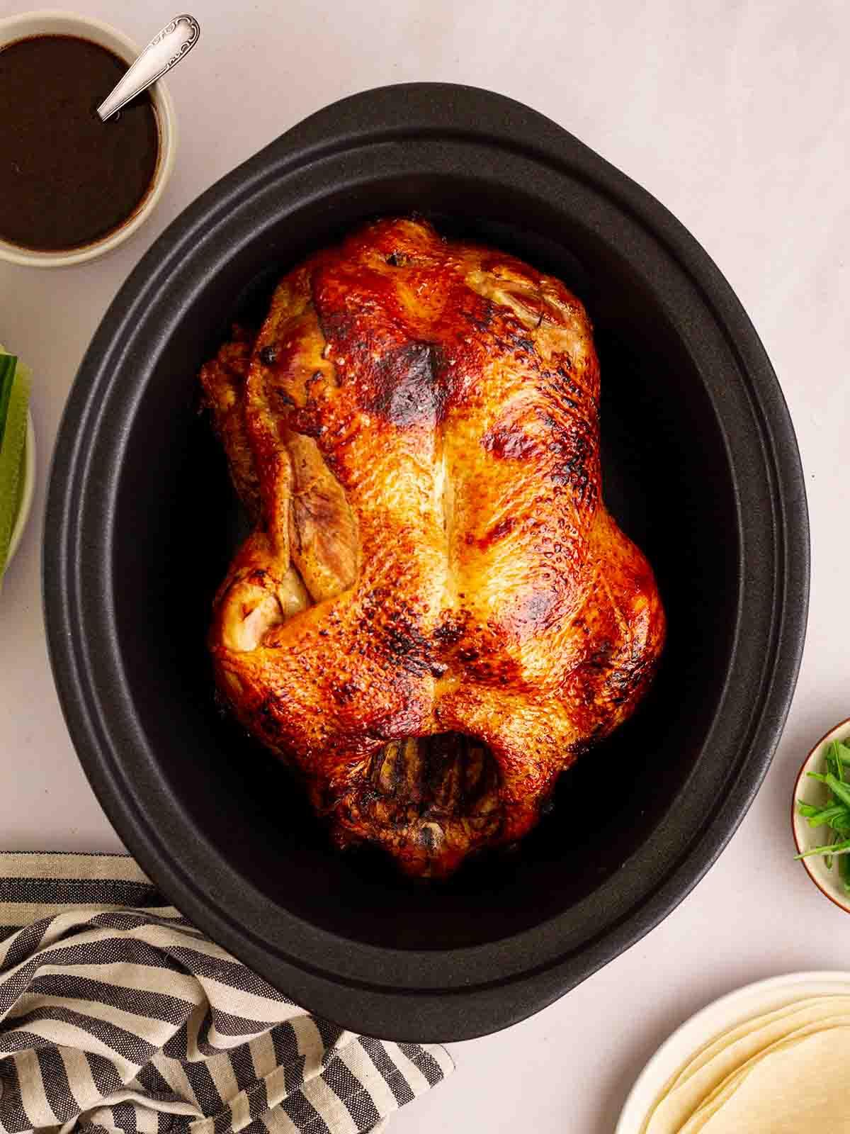 Anatra alla pechinese in pentola a cottura lenta 9 Una slow cooker con un'anatra rosolata all'interno per la ricetta Anatra in Stile Pechinese. Una ciotola di salsa a lato.