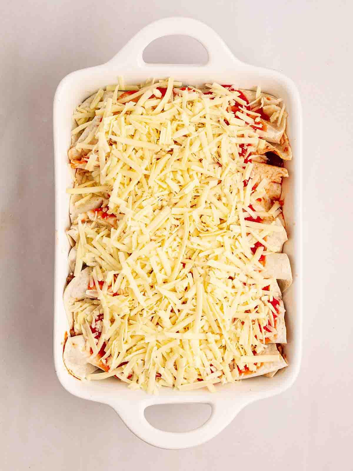 Enchiladas di Manzo 10 Una pirofila da forno con tortillas arrotolate e formaggio grattugiato sopra per il passo 6 della ricetta delle Enchiladas di Manzo.