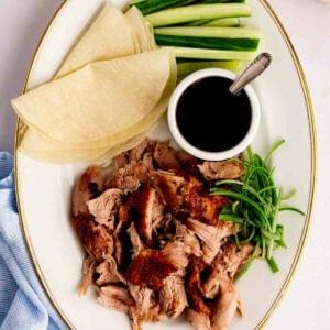 Anatra alla pechinese in pentola a cottura lenta 10 Un piatto con anatra in stile pechinese croccante, cotta nella slow cooker, con crepes, salsa, cetrioli e cipollotti a lato.