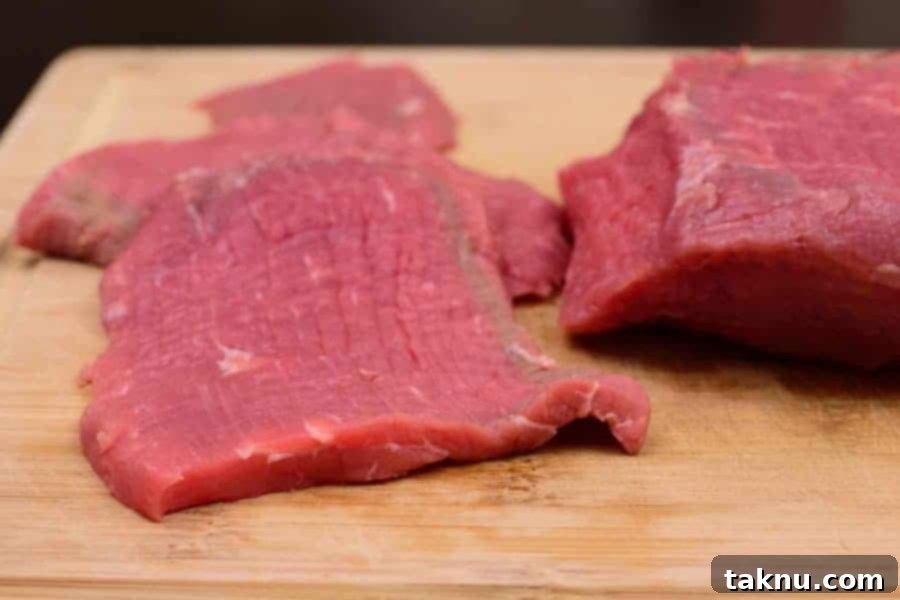 Lean Eye of Round Roast sliced into thin, uniform strips, ready for marinating.