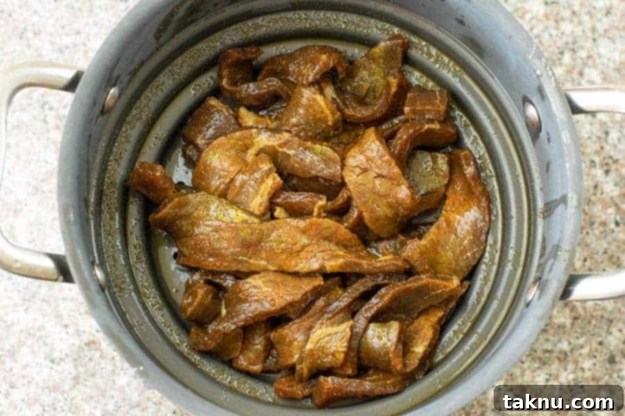 Teriyaki beef jerky strips strained in a colander, removing excess marinade.