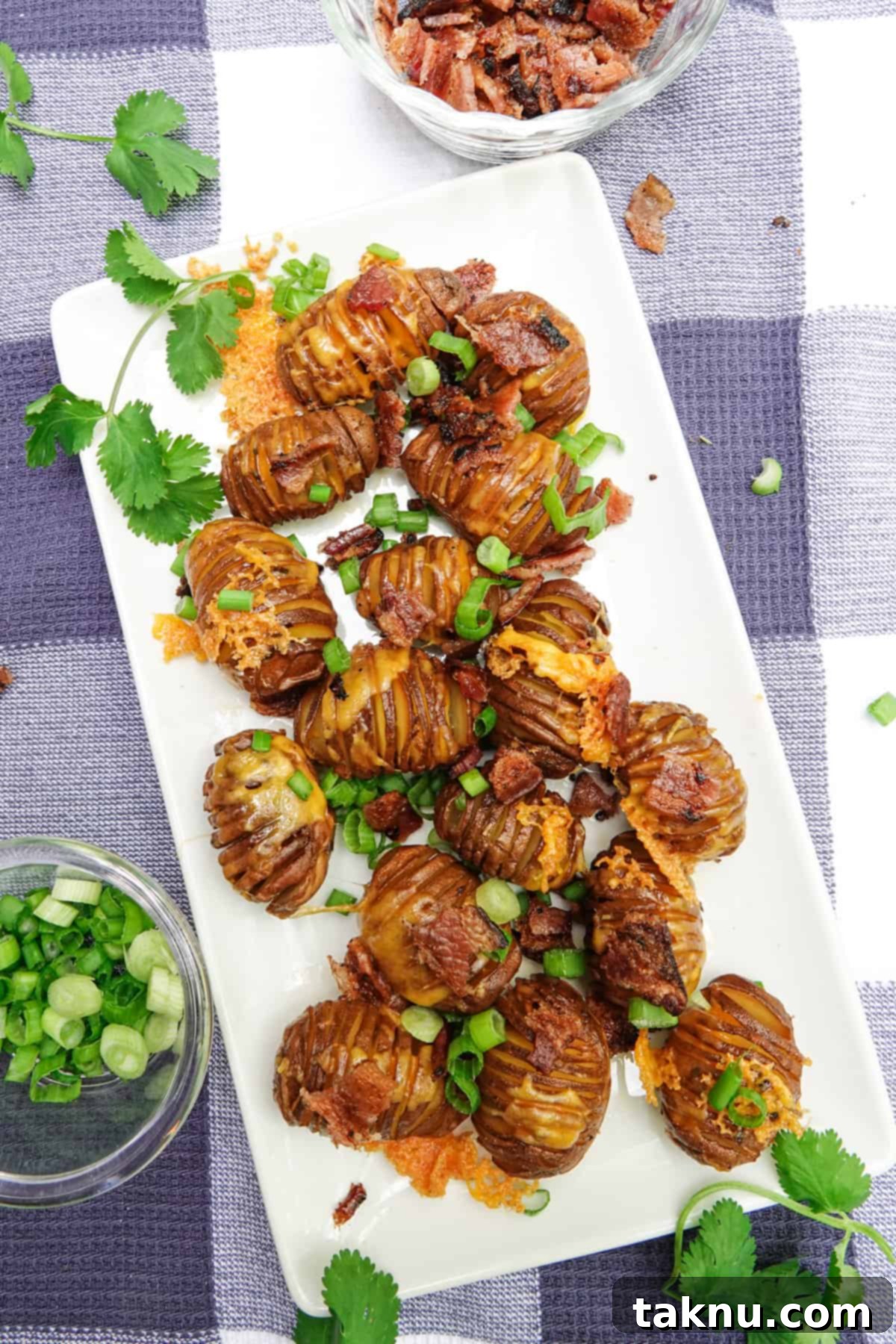 A serving dish filled with golden smoked hasselback potatoes, adorned with melted cheese, crispy bacon bits, and fresh green onions.
