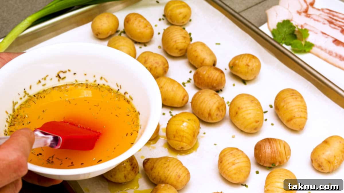 Melted butter being brushed onto pre-sliced hasselback potatoes on a baking sheet before smoking.