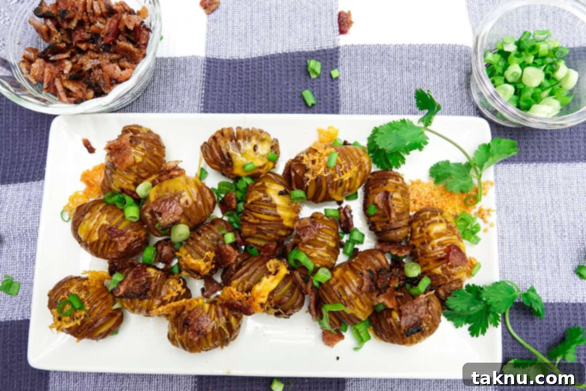 Plated smoked hasselback potatoes garnished with bacon and green onions, served on a white dish with small bowls of toppings.