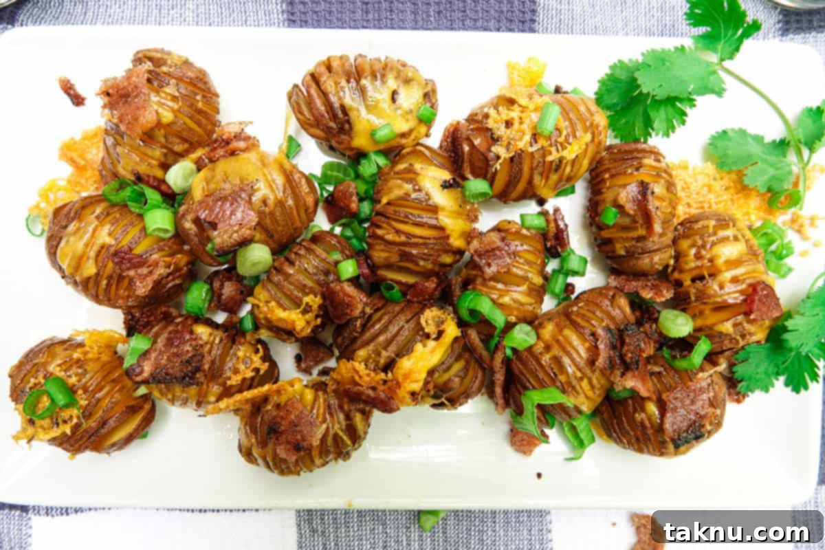 Hasselback potatoes on white dish with bacon and green onions on top