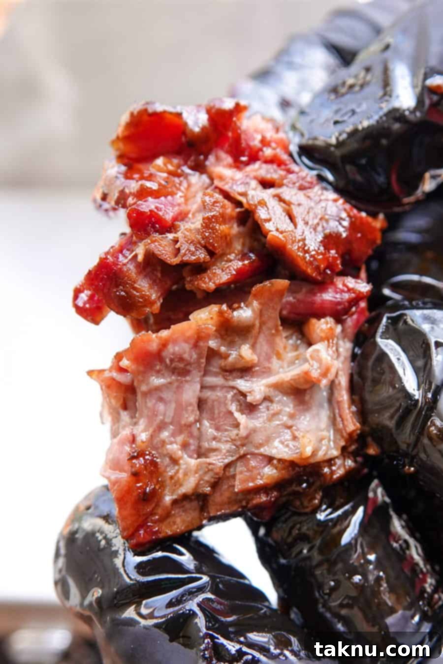 A perfectly smoked burnt end being pulled apart, showcasing its incredible tenderness and smoky crust. A pair of black gloves holds the meat against a soft-focus background, highlighting the succulence of the beef.