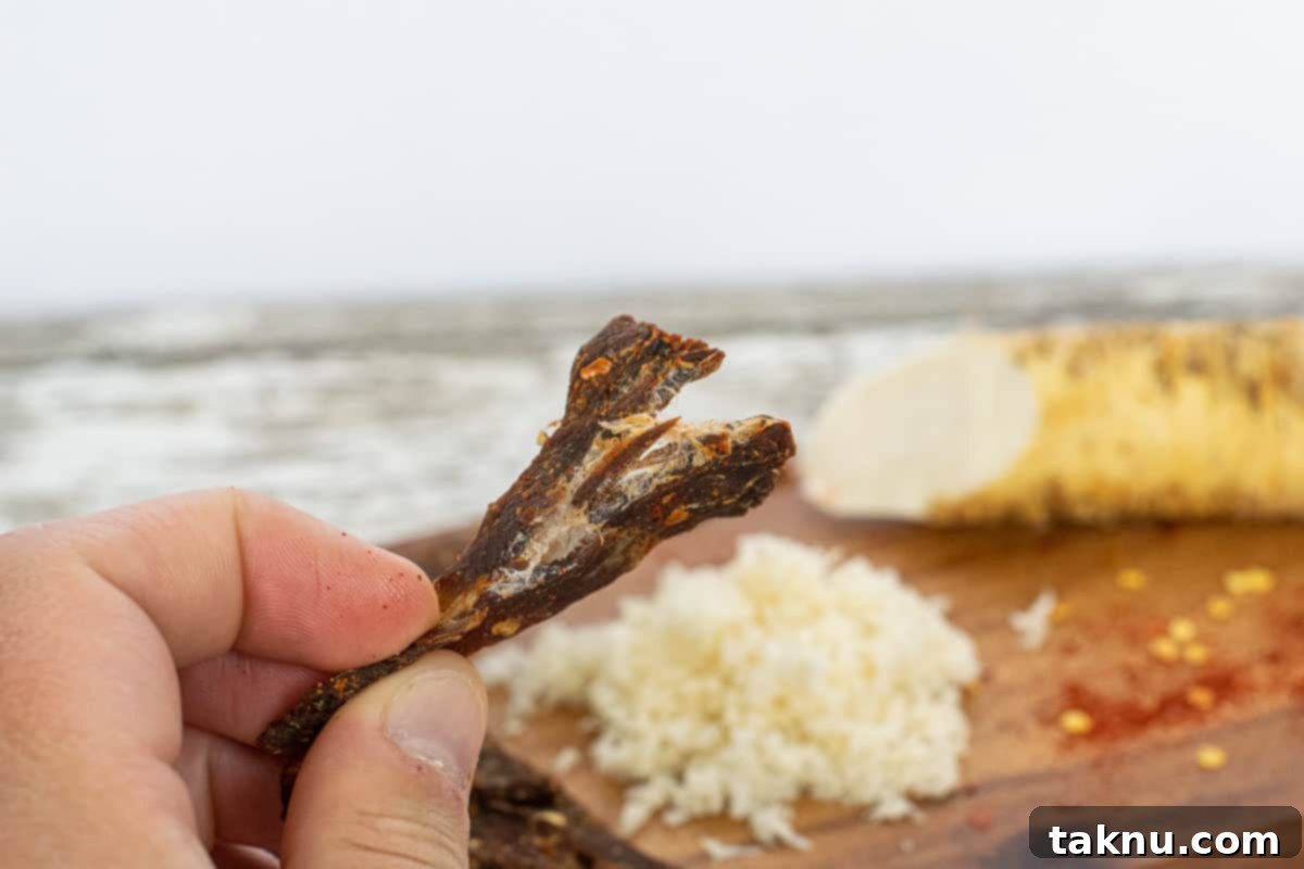 Perfectly finished beef jerky ripped in half, revealing white fibers, with grated horseradish in the background