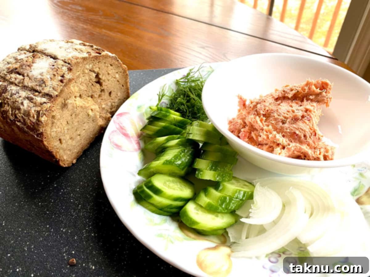 Signature Smoked Salmon Dip 4 A vibrant platter featuring a generous bowl of smoked salmon dip, surrounded by crisp cucumber slices, thinly sliced red onions, and seeded bread, perfect for a refreshing party spread.
