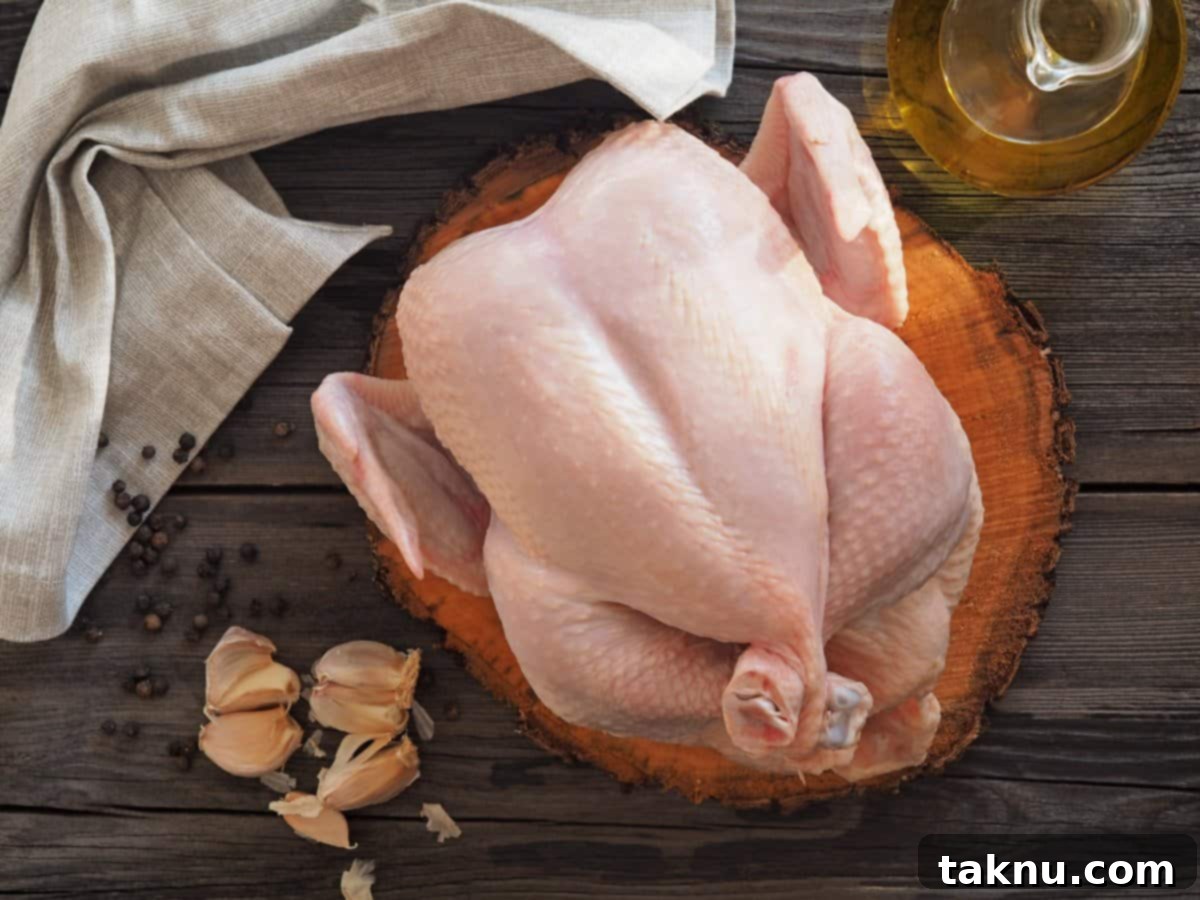 Raw roaster chicken on cutting board with garlic and bottle of olive oil