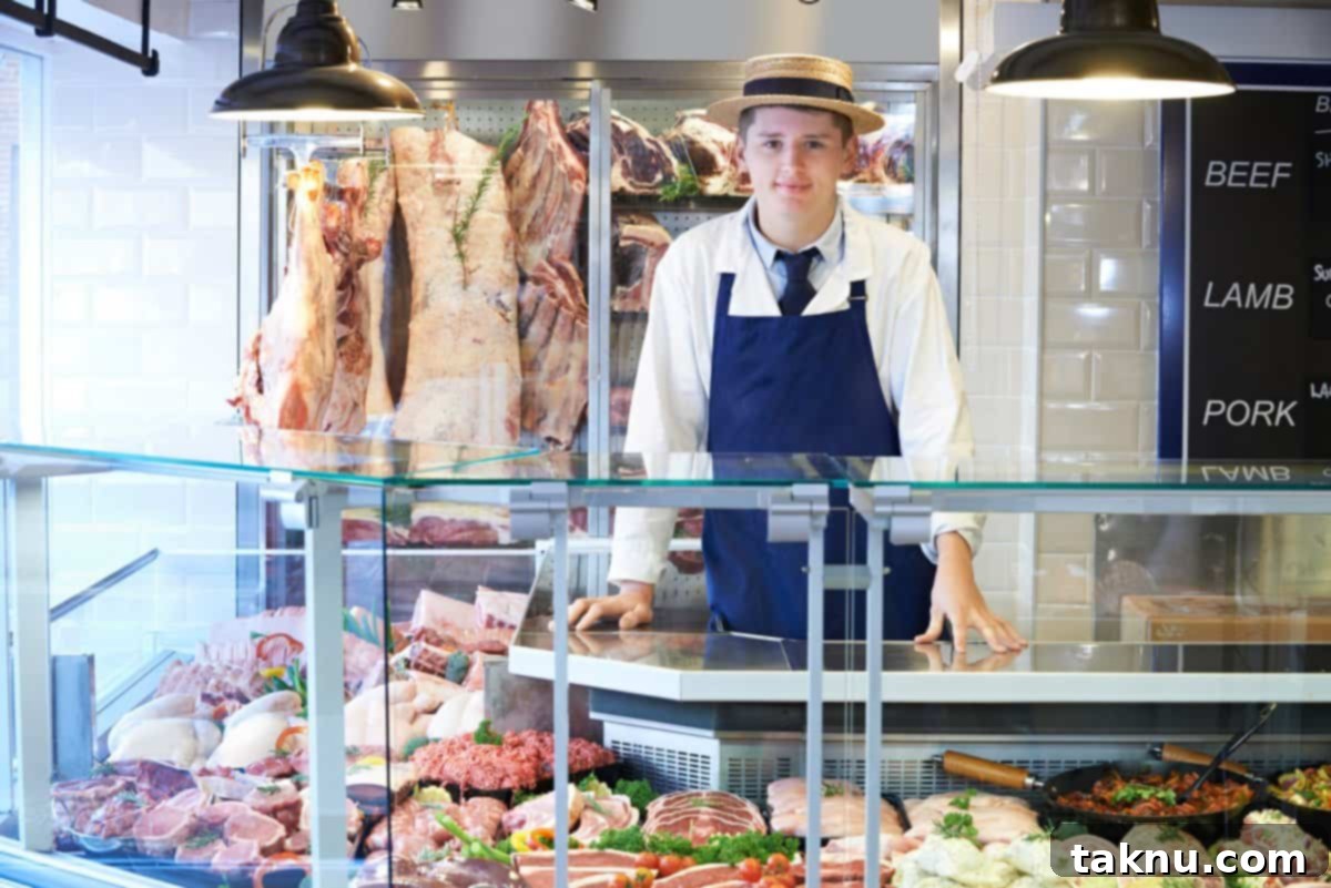 Tomahawk Steak Perfection 5 A friendly butcher in an apron and hat stands proudly behind a display of fresh meats in a well-stocked butcher shop.