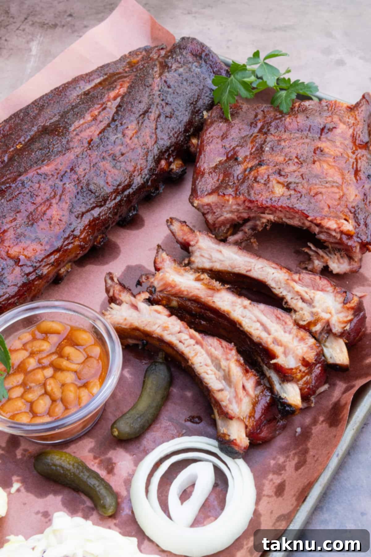 A perfectly smoked rack of 3-2-1 ribs resting on a platter, accompanied by sliced onions, baked beans, and pickles, ready to be served.