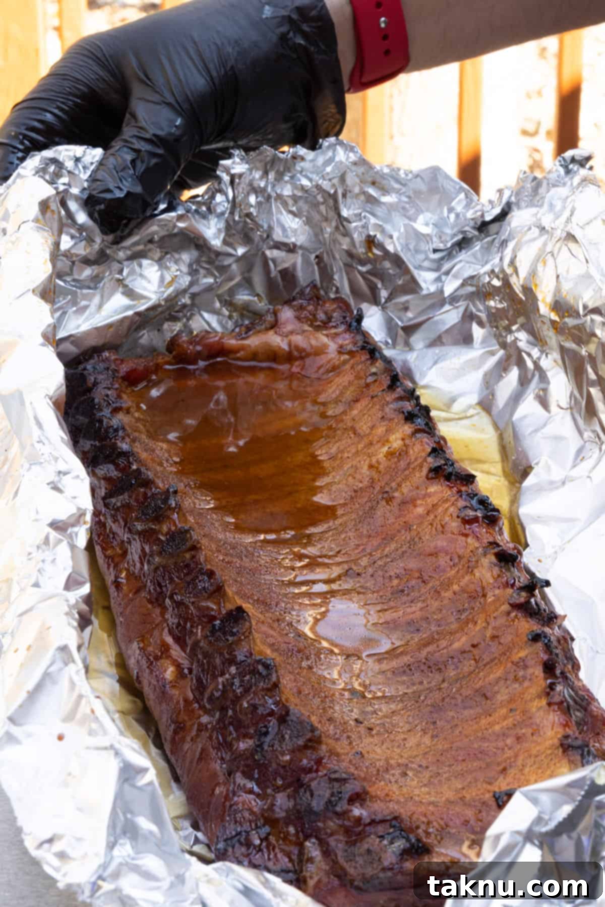 A rack of pork ribs inside a large piece of aluminum foil, with apple juice and honey being poured over it before wrapping.