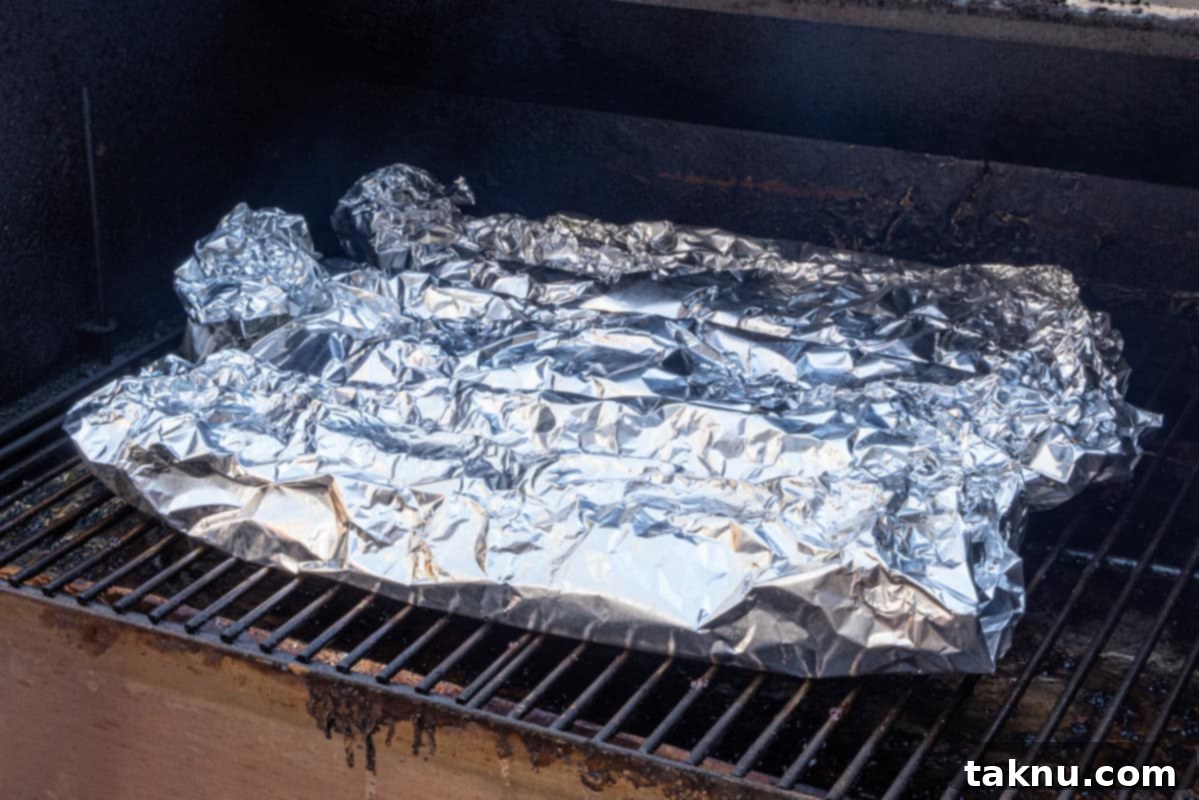Three racks of pork ribs, each individually wrapped in aluminum foil, placed back on the smoker grates for the tenderizing phase.