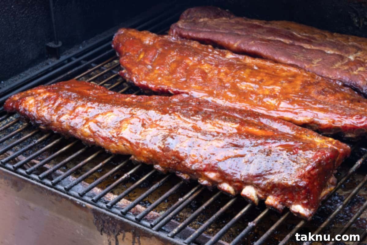 Three racks of 3-2-1 smoked ribs, glistening with BBQ sauce, cooking on the smoker grates during the final hour.