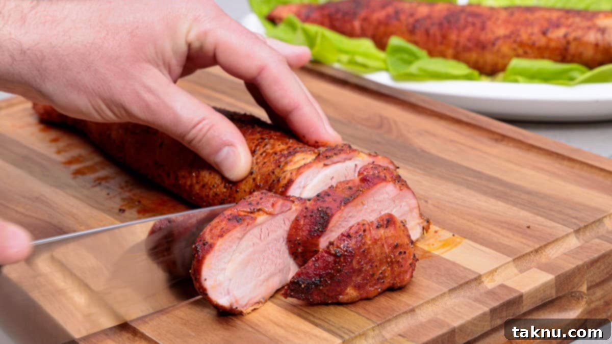 Slicing a perfectly cooked pork tenderloin on a wood cutting board with a sharp chef's knife.