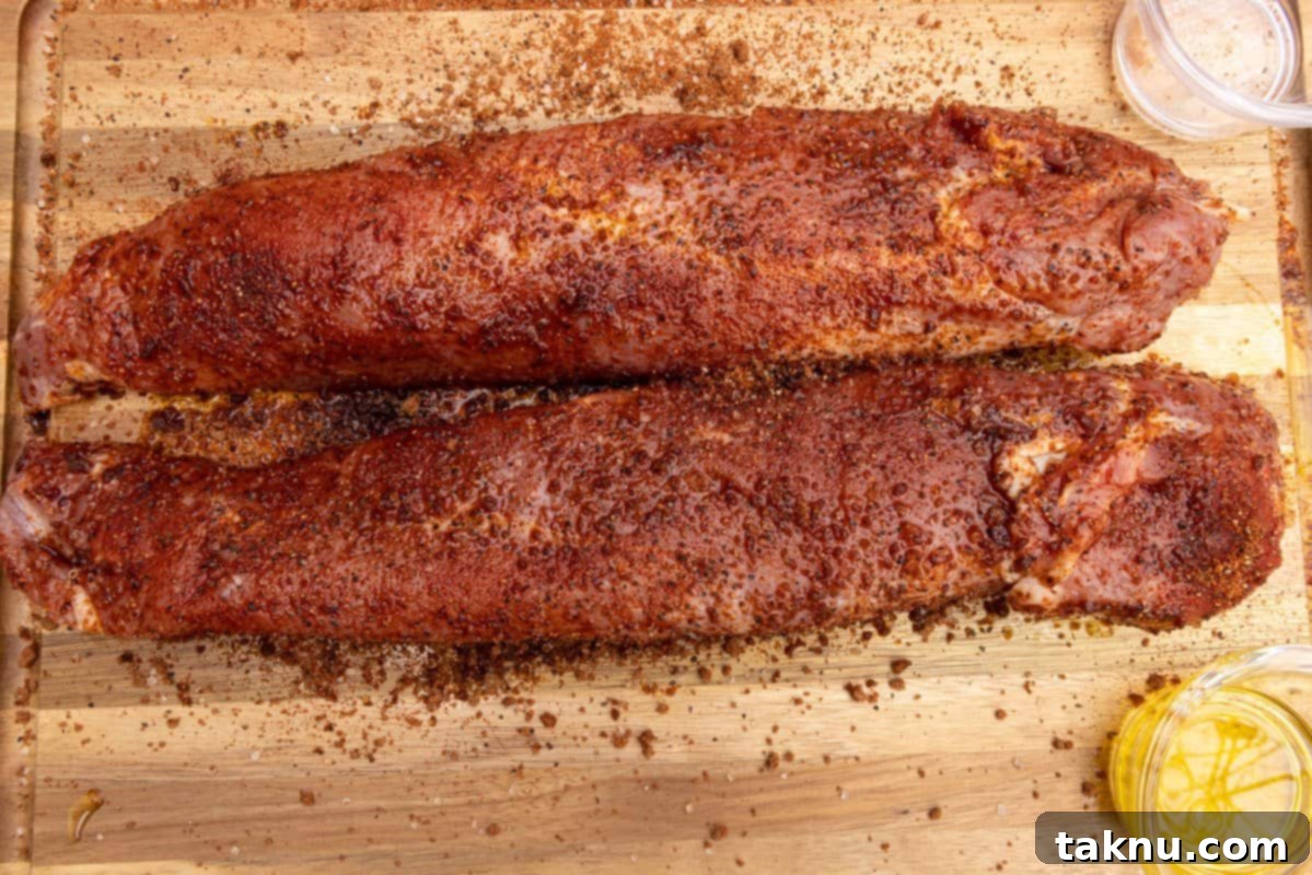 Two pork tenderloins generously seasoned with dry rub on a wood cutting board.