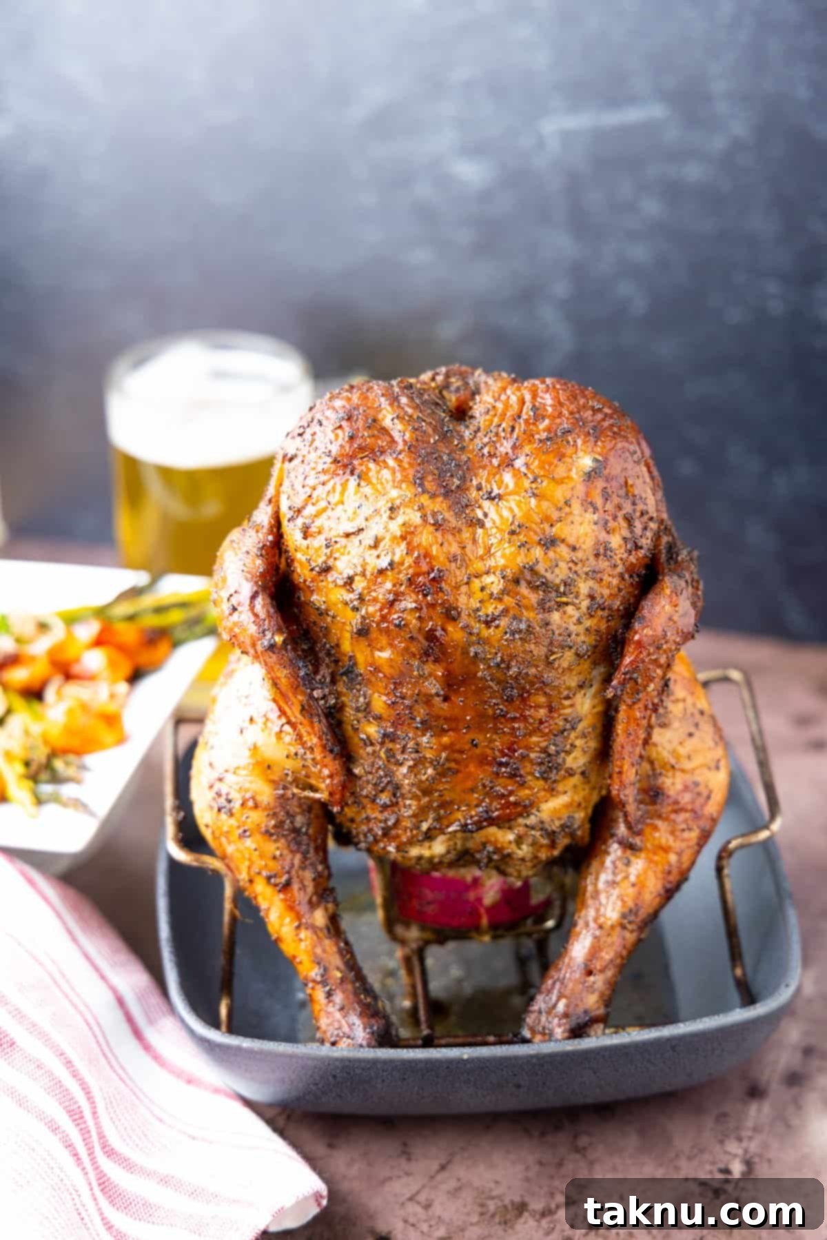 Ultimate Smoked Beer Can Chicken 11 Beautifully smoked beer can chicken on a stand with a dark background and a frosty glass of beer, perfectly ready to serve.