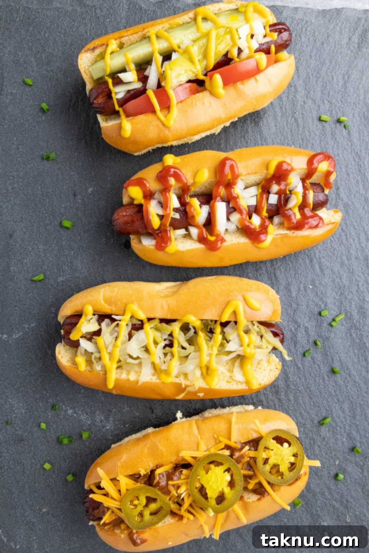 Four perfectly smoked hot dogs on a grey slate, each adorned with delicious and diverse toppings, showcasing their crispy exterior and inviting presentation.