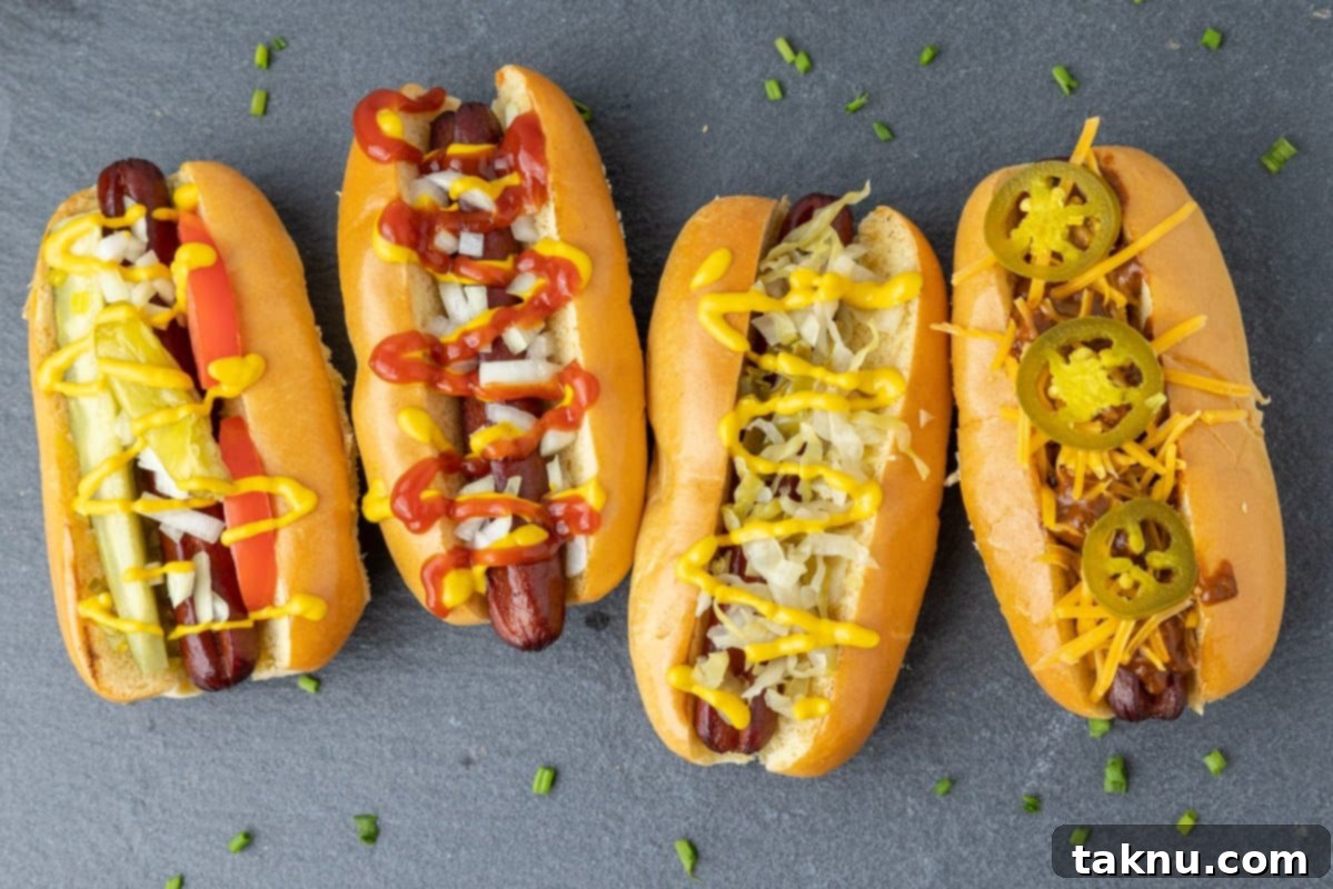 Four smoked hot dogs with different toppings artfully arranged on a grey slate, inviting a delicious tasting experience.