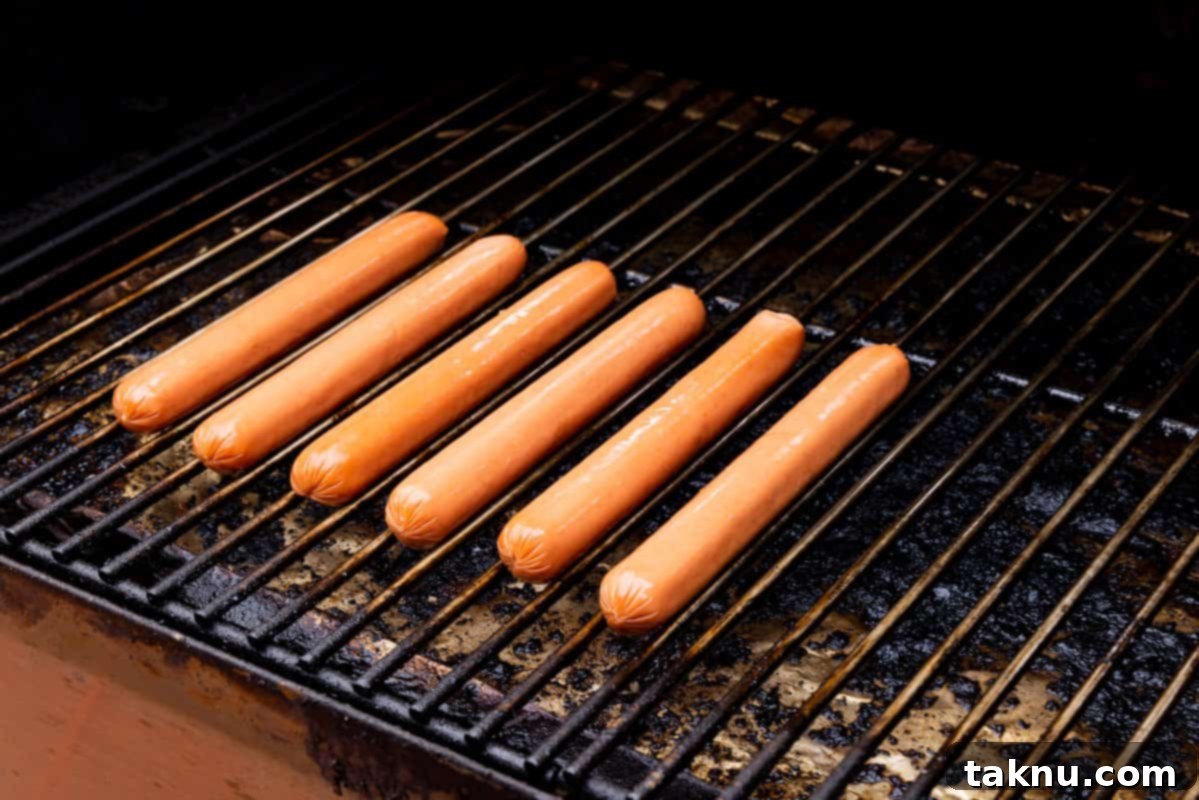 Six sizzling hot dogs evenly spaced on a hot grill grate, showing perfect grill marks and inviting char.