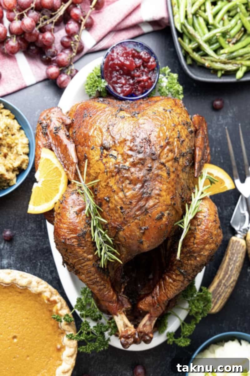 Crispy Skinned Smoked Turkey Masterpiece 2 A perfectly smoked turkey on a white platter, surrounded by traditional holiday side dishes like pumpkin pie, green beans, and lemons.