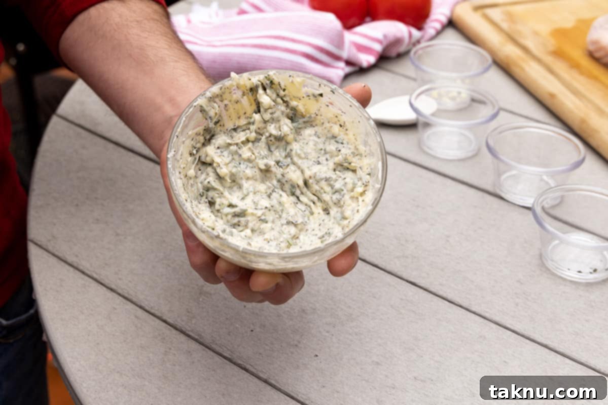 Crispy Skinned Smoked Turkey Masterpiece 6 A man's hand holding a bowl of seasoned butter, perfectly mixed with herbs, over a table, ready for application.