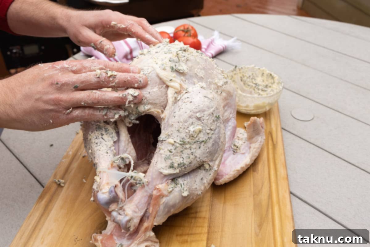 Crispy Skinned Smoked Turkey Masterpiece 7 Hands applying seasoned butter liberally to a raw turkey on a cutting board, ensuring full coverage for flavor and crispy skin.