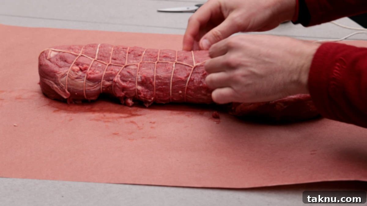 Meat roast on butcher paper being trussed with butcher twine.