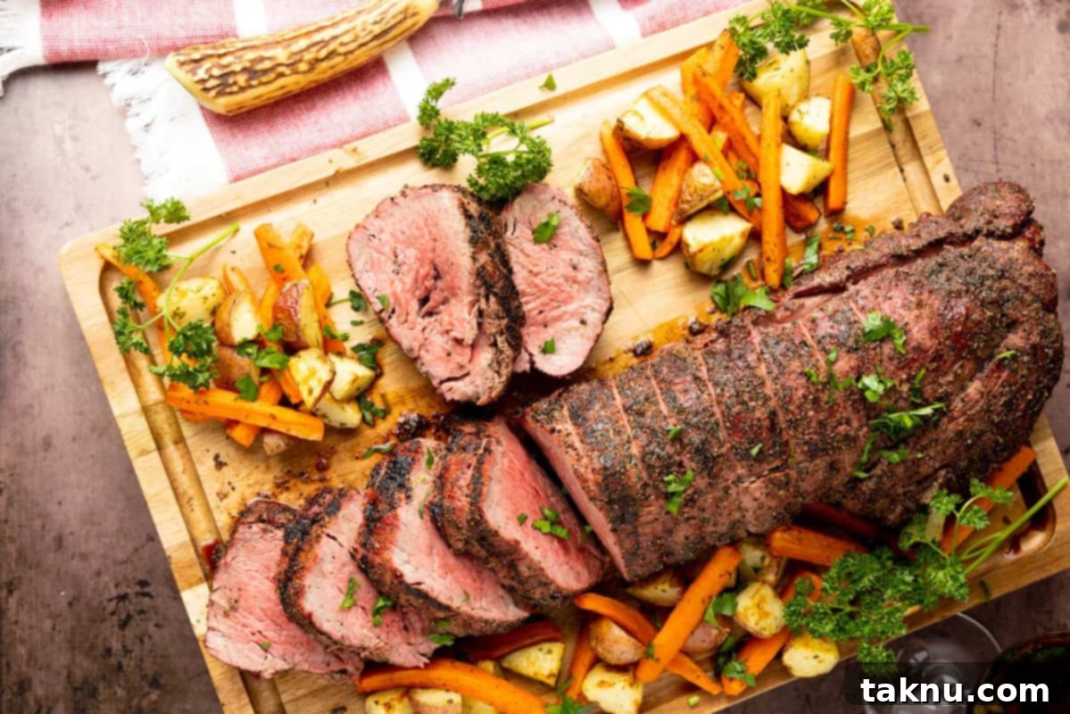 Beef tenderloin sliced on cutting board with potatoes and carrots surrounding meat.