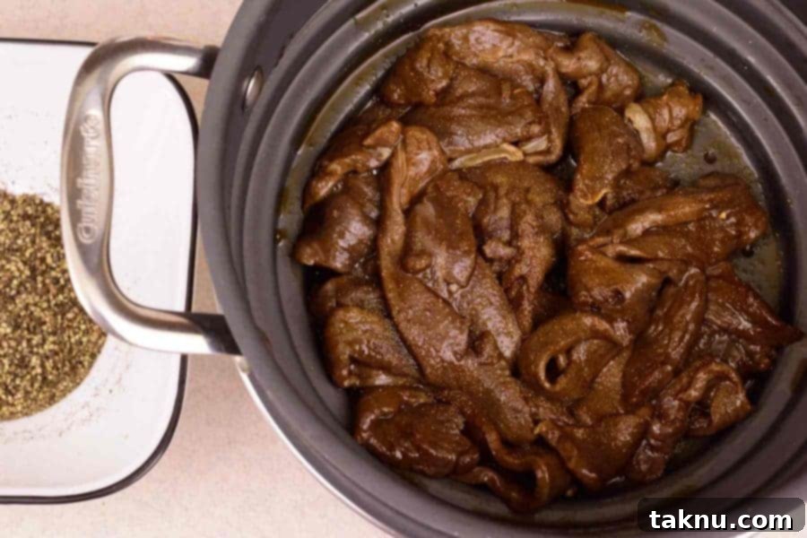 Marinated deer meat for jerky drained in colander next to bowl of pepper