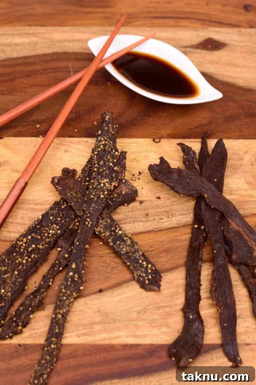 Jimmy's Teriyaki Deer jerky on a cutting board with teriyaki sauce and chopsticks.