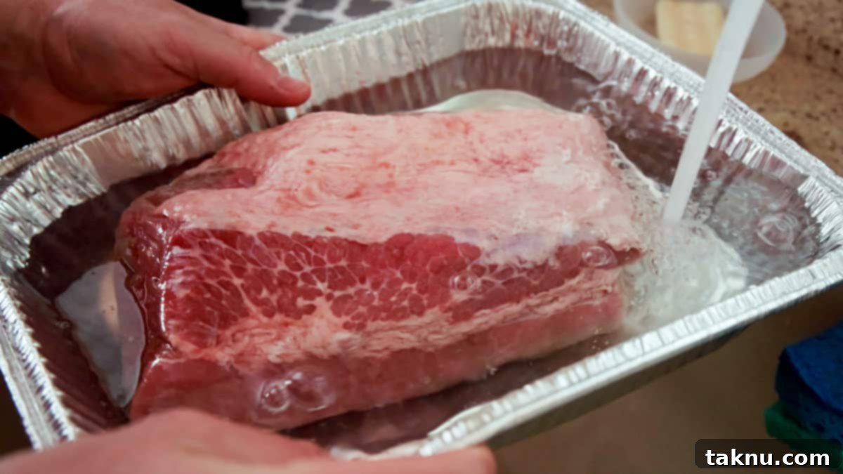 Slow-Smoked Corned Beef 4 Raw corned beef brisket soaking in cold water within an aluminum pan, a crucial step for reducing saltiness.