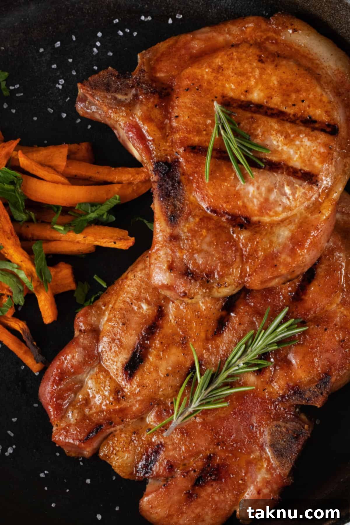 Perfect Traeger Pork Chops 2 Two perfectly grilled Traeger smoked pork chops garnished with fresh rosemary and carrots on a black plate, ready to serve.