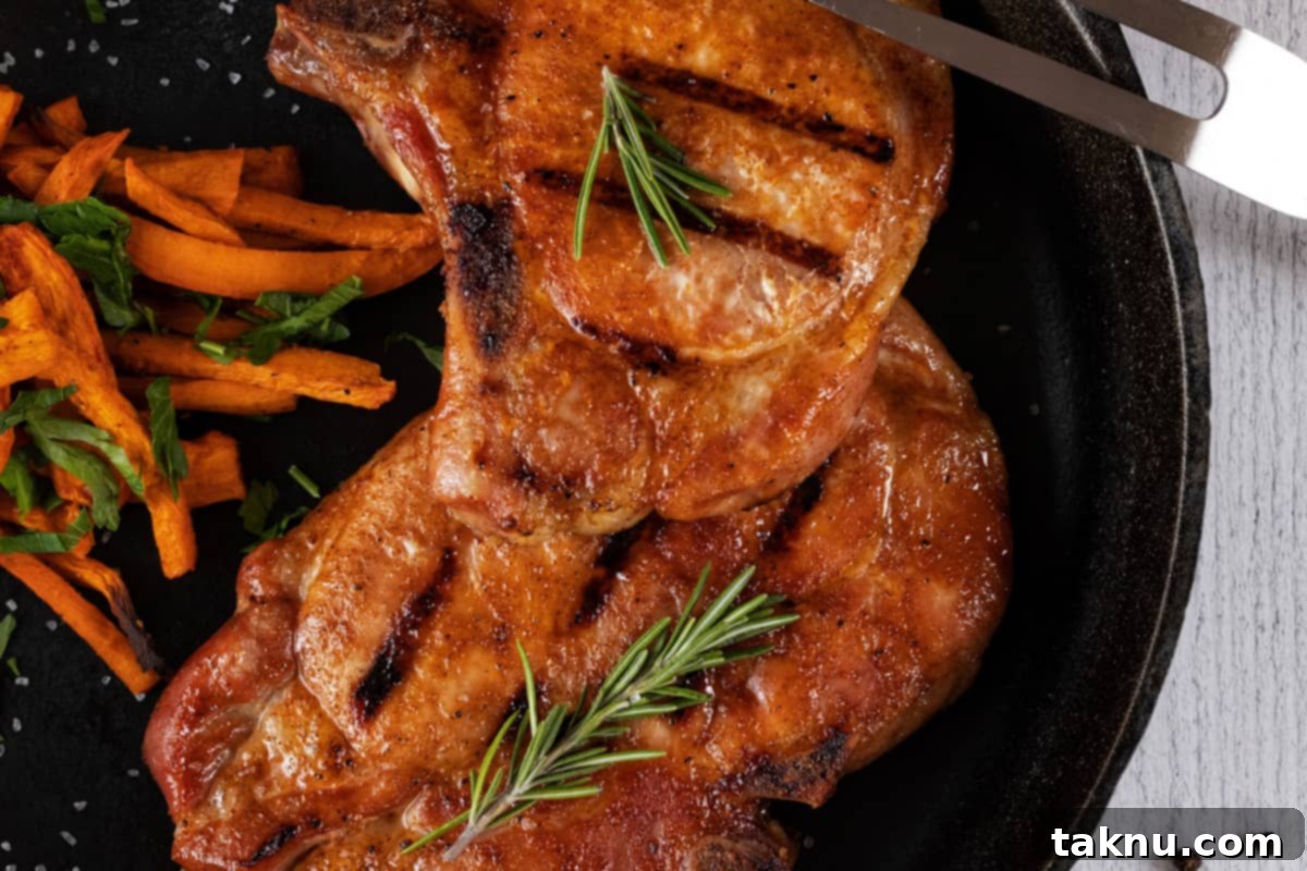 Perfect Traeger Pork Chops 9 Two beautifully smoked pork chops resting on a wooden cutting board with fresh rosemary, highlighting their golden-brown crust and juicy appearance.