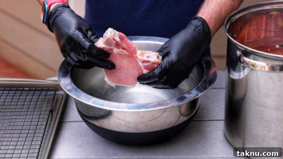 Perfect Traeger Pork Chops 4 A chef's gloved hand gently rinsing a brined pork chop under cool running water in a silver bowl.