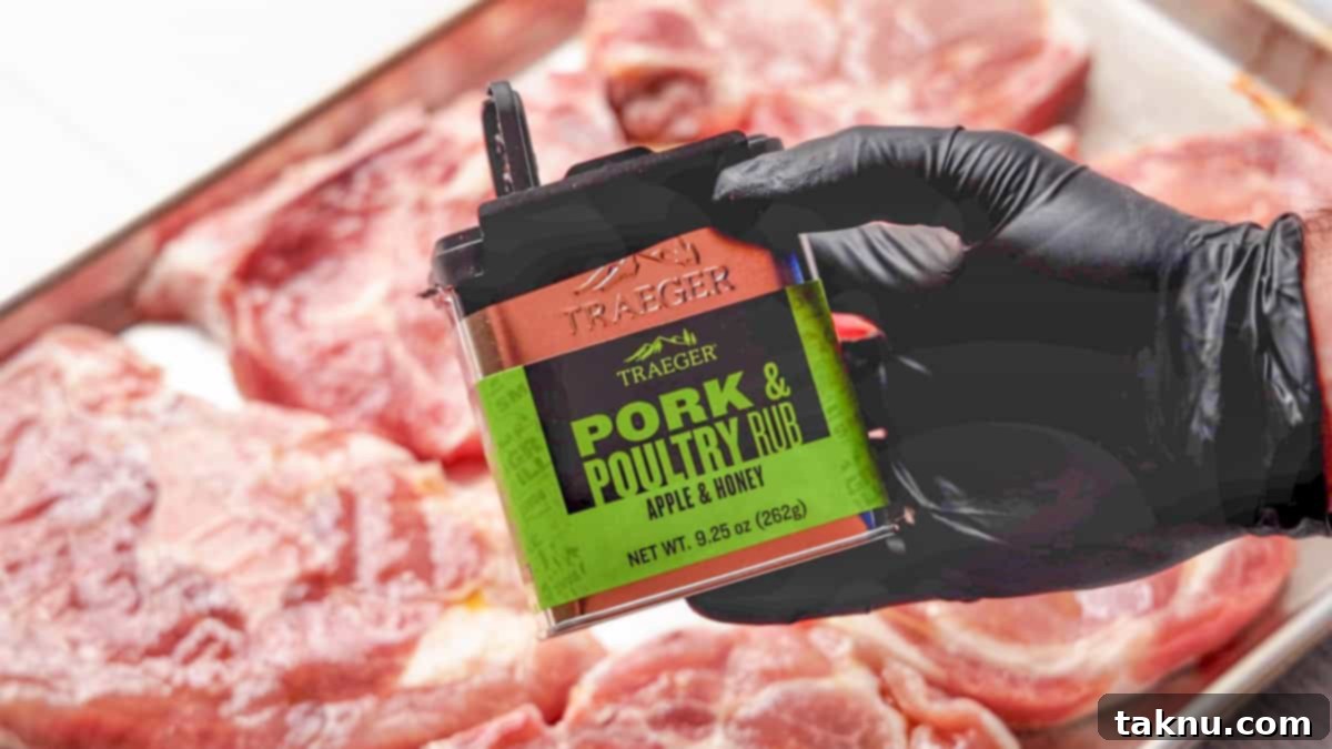 Perfect Traeger Pork Chops 5 A hand in a black latex glove holding a can of Traeger pork seasoning over several raw pork chops arranged on a baking sheet, ready for seasoning.