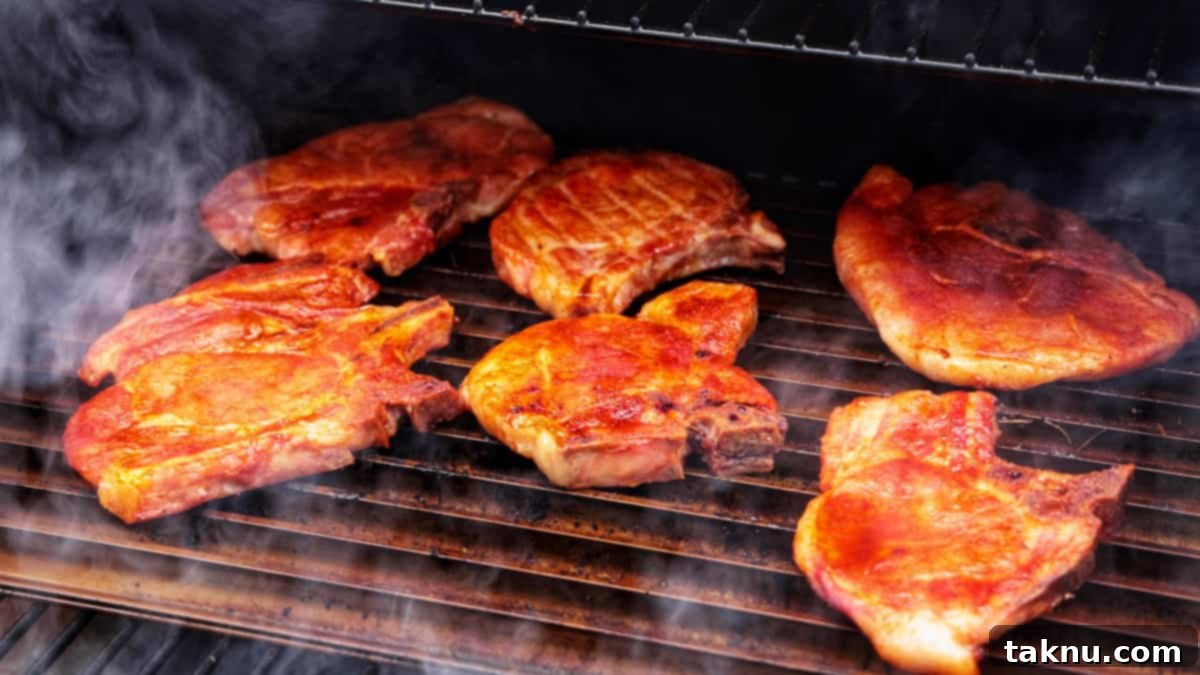 Perfect Traeger Pork Chops 7 Several thick-cut pork chops grilling on the grates of a pellet smoker, enveloped in wisps of smoke as they cook.