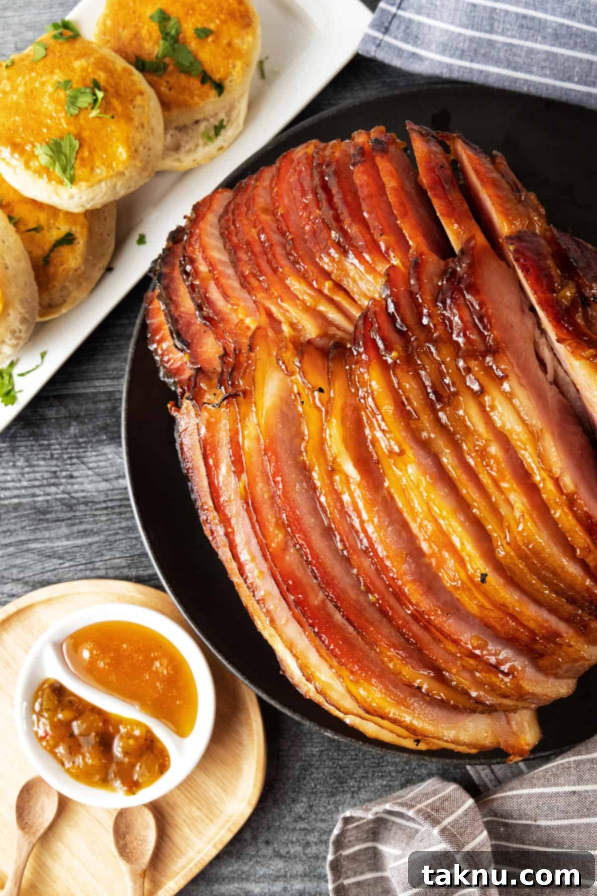 Sweet Apricot Smoked Ham 2 A beautifully smoked spiral ham on a black platter, garnished and ready to serve, with biscuits and jam in the background.
